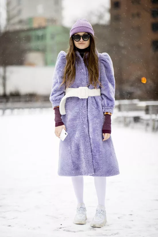 Девушка в фиолетовом меховом пальто с белым поясом, шапочка и кроссовки