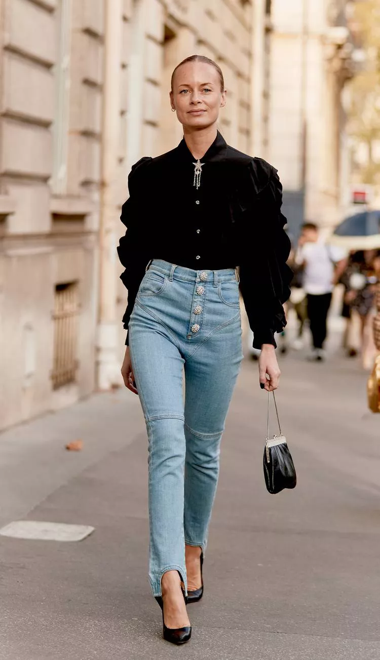 Девушка в голубых джинсах с высокой талией, черная блузка с пышными рукавами и черные туфли