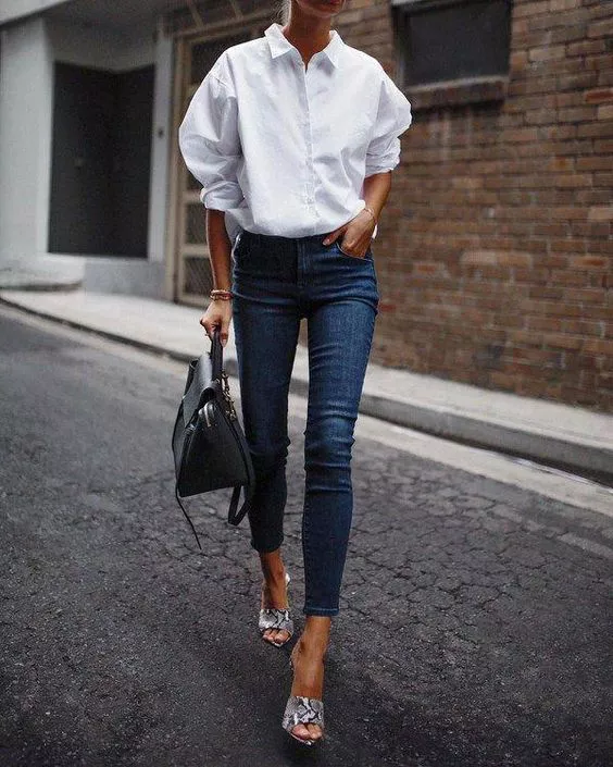Девушка в синих узких джинсах, белая рубашка и сумка