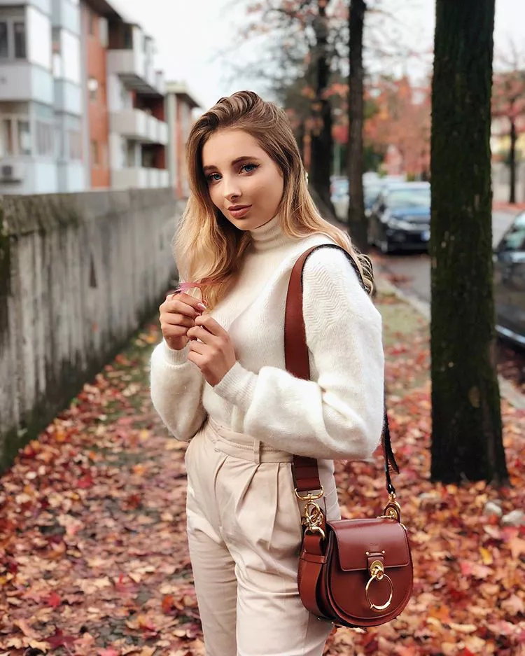 Девушка в светлых брюках, белый свитер и коричневая сумка