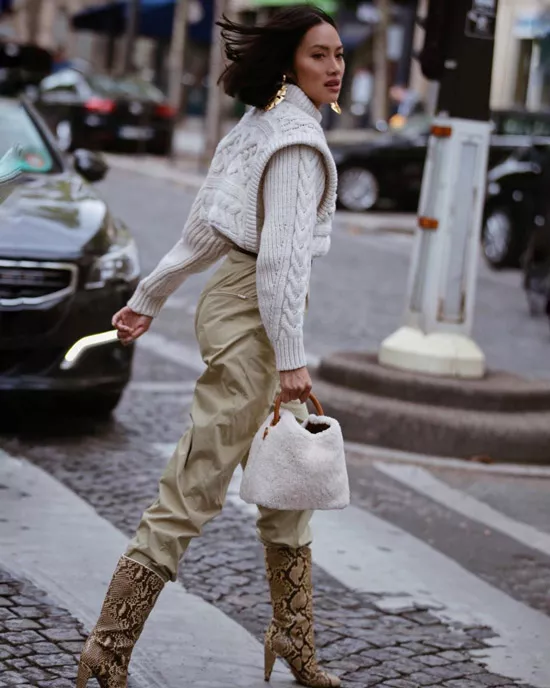 Девушка в бежевых брюках, бежевый свитер и сапоги со змеиным принтом