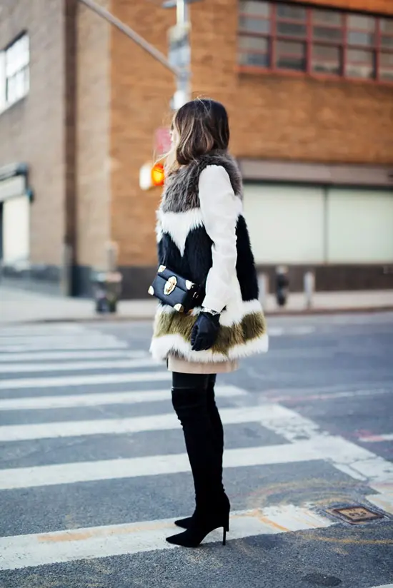 Девушка в черных замшевых ботфортах, меховая жилетка и квадратная сумочка