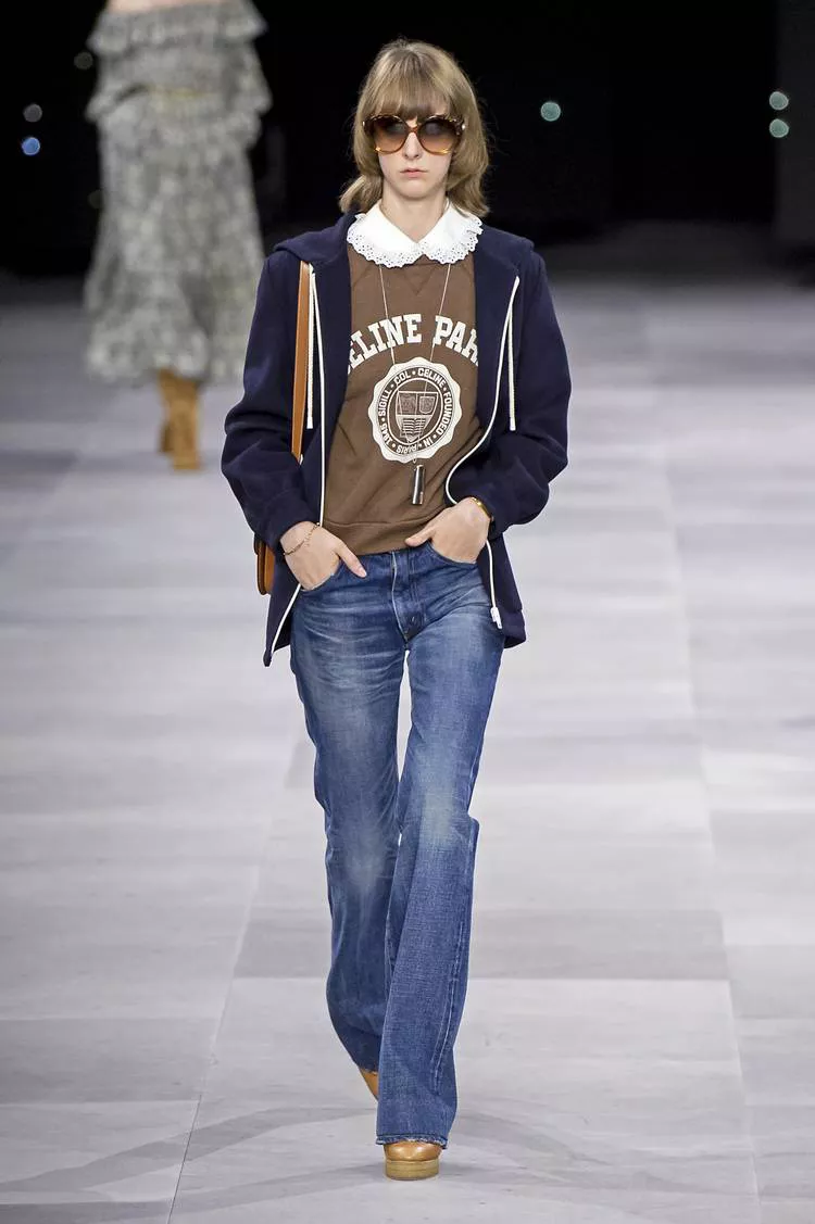 Модель в синих джинсах клеш, коричневая толстовка и темная кофта