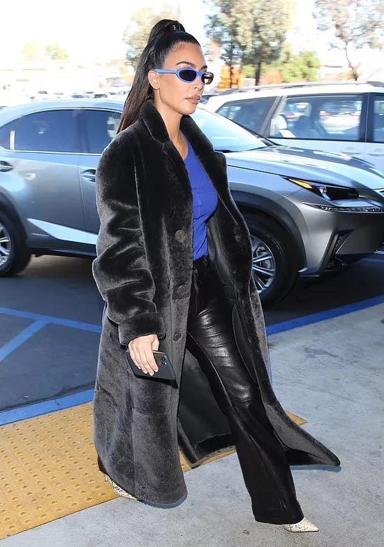 Ким Кардашьян в кожаных брюках, синем топе, очках и плюшевом пальто
