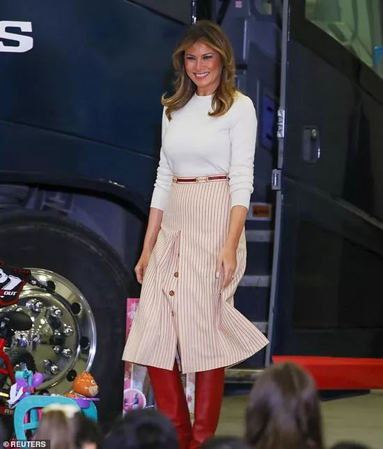 Мелания Трамп в белом джемпере, юбке в полоску и красных сапогах