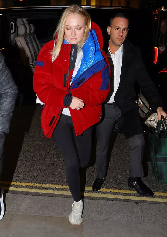 Софи Тернер в красной оверсайз-куртке и черных леггинсах