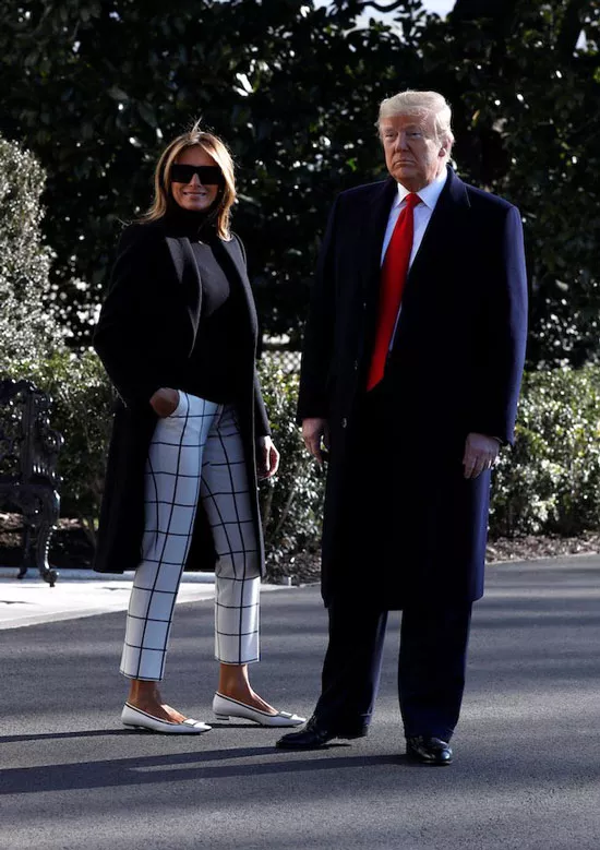 Мелания Трамп в белых брюках в клетку, черном пальто и белых туфлях