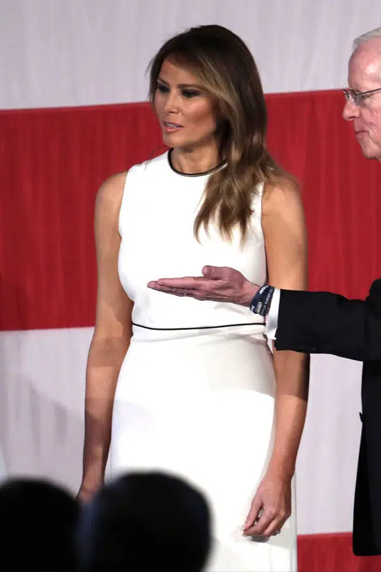 Мелания Трамп в белом платье без рукавов с с черной полоской на талии