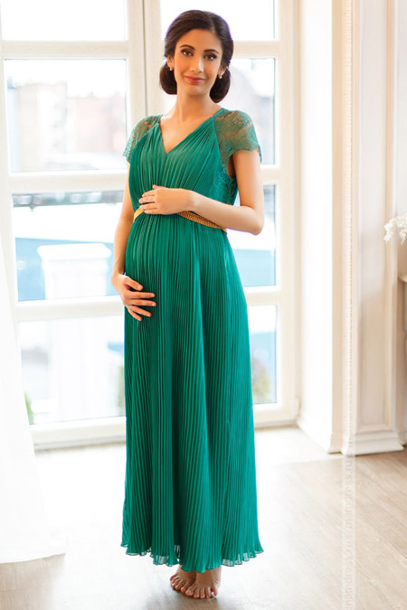 Девушка в длинном платье для беременных плиссе зеленого цвета