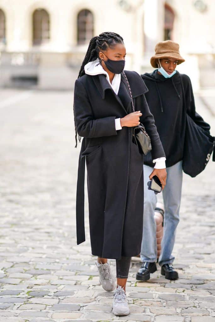 Девушка в черном шерстяном пальто с поясом, белая толстовка и кеды
