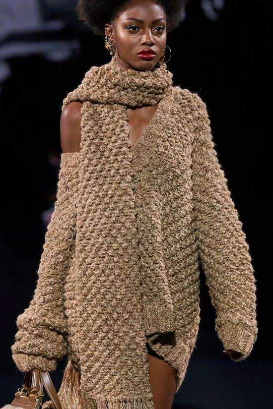 Модель в коричневом вязанном платье мини с шарфом