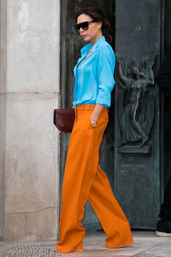 Виктория Бекхэм в оранжевых широких брюках, голубая рубашка и клатч