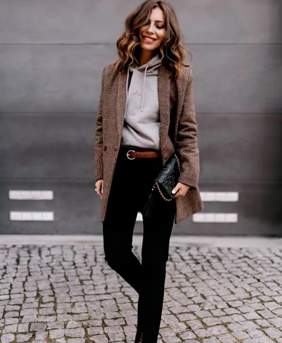 Девушка в черных джинсах с ремнем, серая толстовка и коричневый удлиненный пиджак