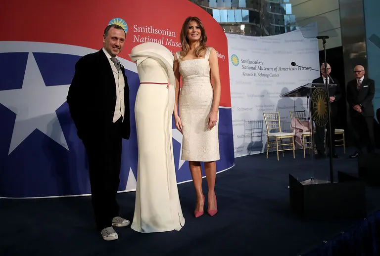 Мелания Трамп в белом платье футляр ниже колен с открытыми руками