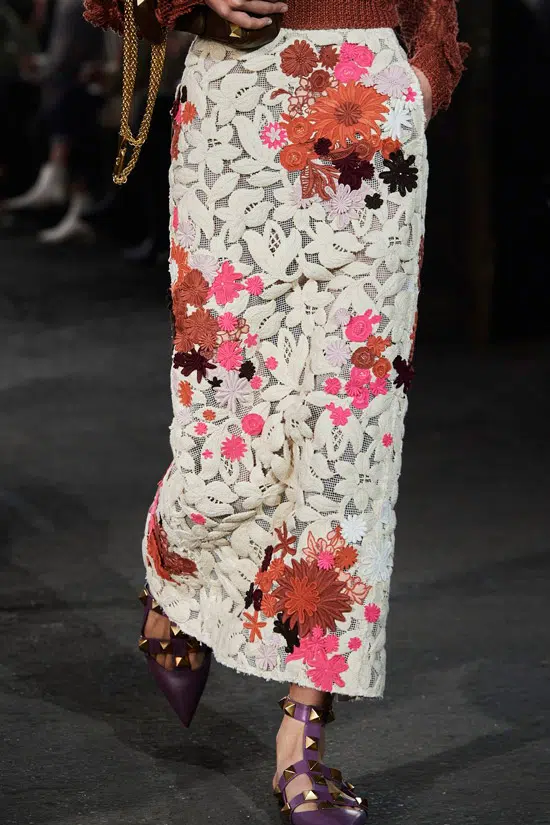 Модель в белой узкой юбке с цветочным принтом и бордовые сандалии