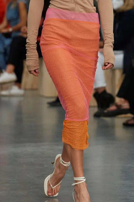 Модель в оранжевой облегающей юбке, белые босоножки на каблуке