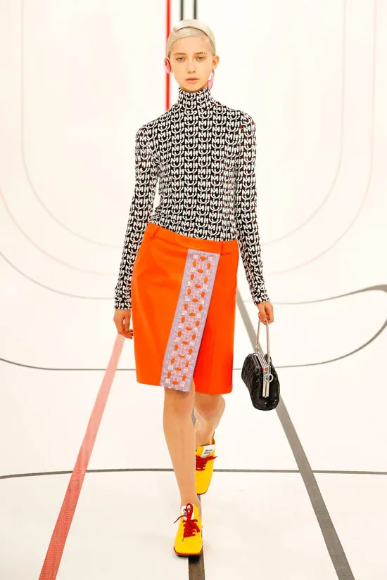 Модель в пестрой водолазке, оранжевая юбка и желтые кроссовки от miu miu