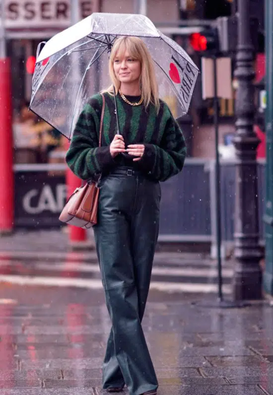 Девушка в кожаных свободных брюках, свитер в черно зеленую полоску и сумочка на плече