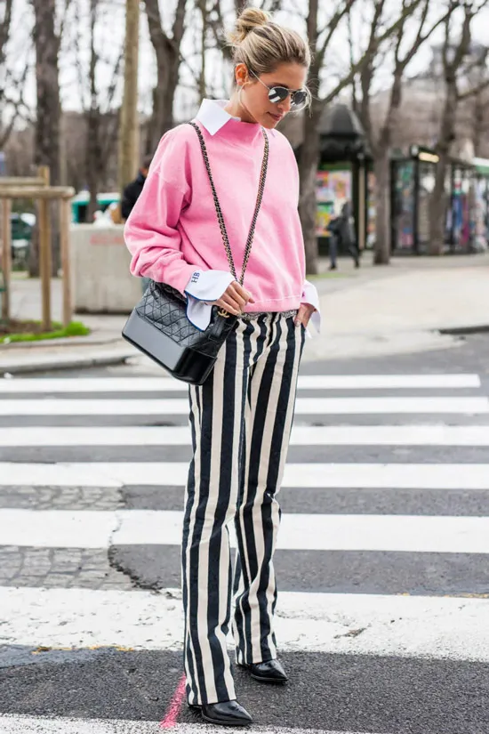Девушка в черно белых брюках в вертикальную полоску, нежно розовый свитер и темная сумка, образ завершают черные туфли на шпильке
