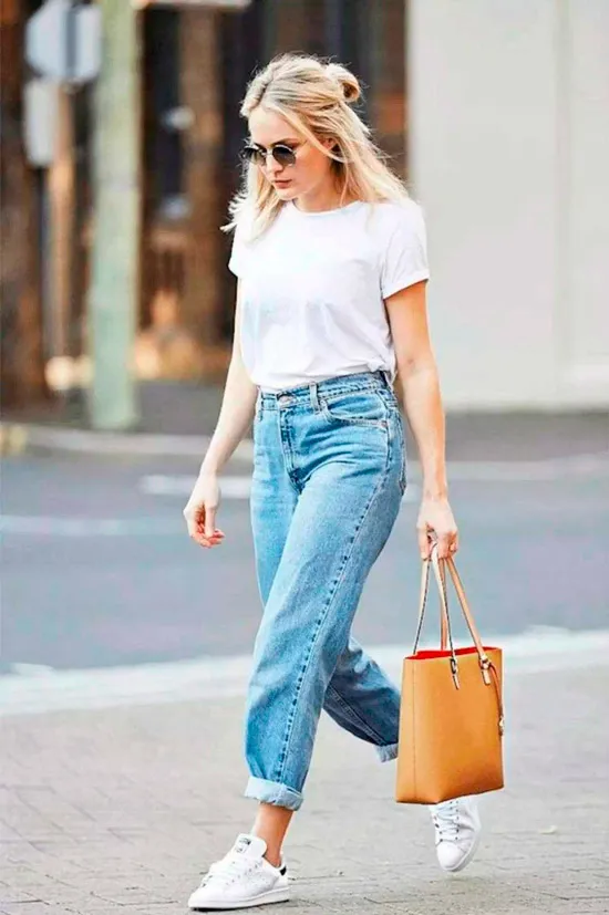 Девушка в голубых прямых джинсах, простая белая футболка, кеды и бежевая сумочка
