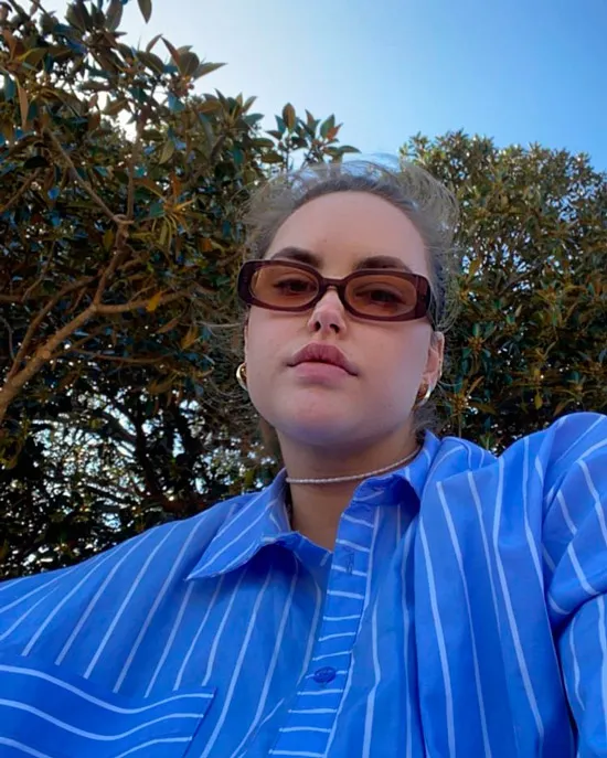 Девушка в голубой рубашке в тонкую полоску и коричневых прямоугольных солнцезащитных очках
