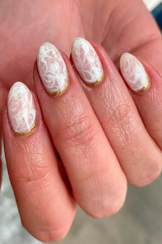Белый мраморный маникюр с золотыми блестками на овальных ногтях