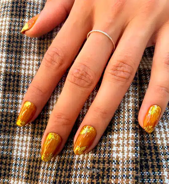 Оранжевый маникюр с золотыми хлопьями на овальных ногтях средней длины