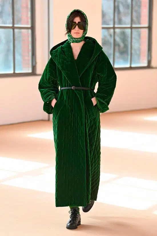 Модель в длинном зеленом пальто с тонким ремнем