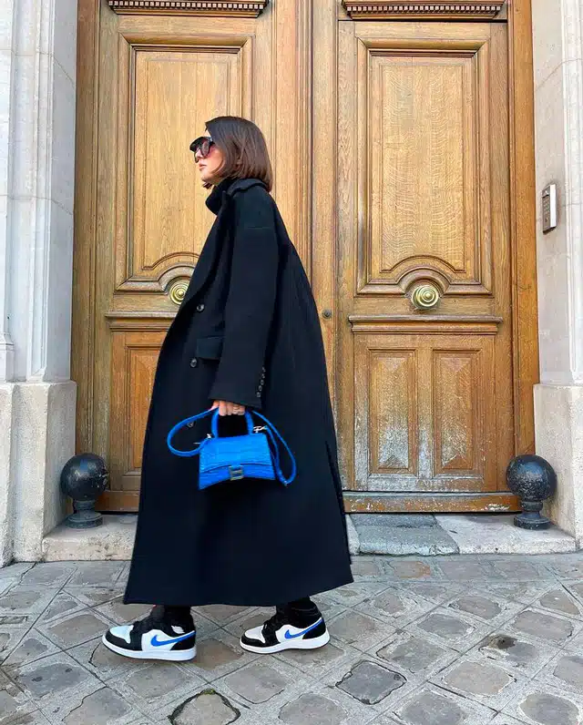 Девушка в черном пальто оверсайз, кроссовках и с синей мини сумочкой