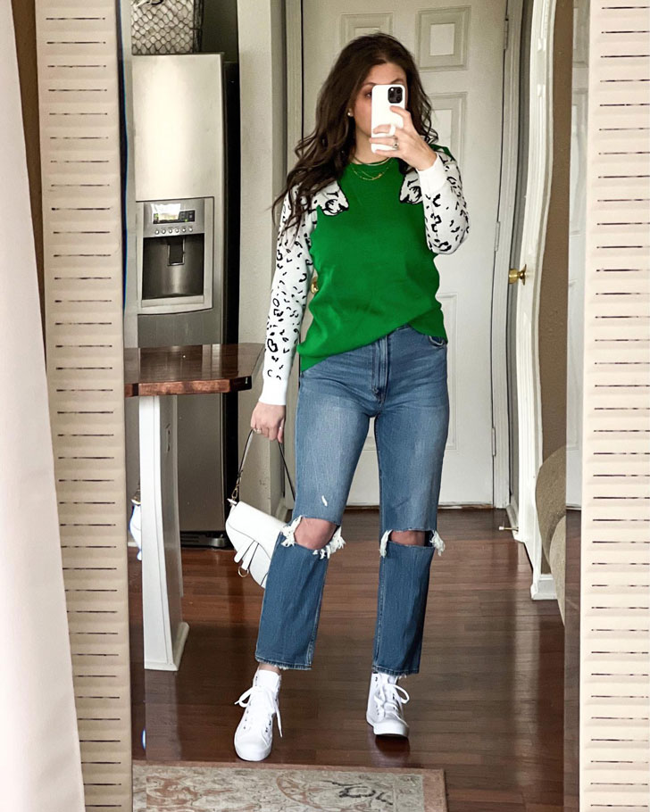 Девушка в рванных джинсах, зеленом свитшоте и белых кедах