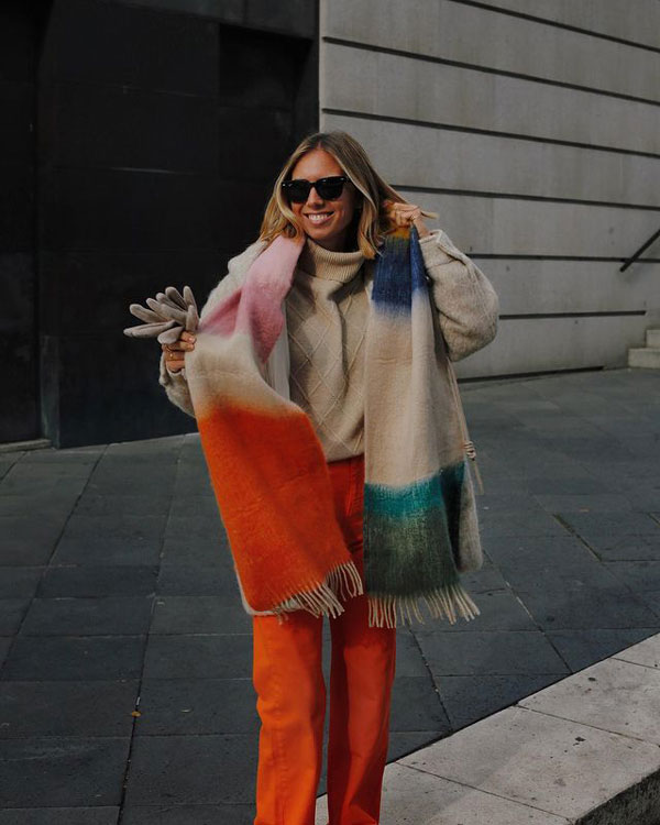 Девушка в прямых оранжевых джинсах, бежевом свитере и с разноцветным палантином