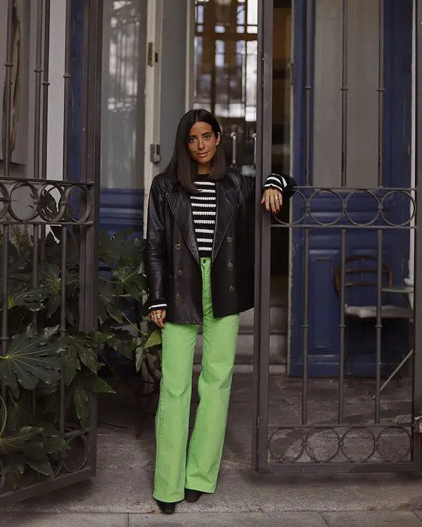 Девушка в светло зеленых джинсах клеш, водолазке с полоску и кожаном пиджаке оверсайз