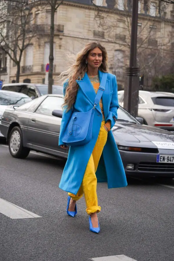 Девушка в ярких желтых джинсах, голубом пальто и туфлях лодочках