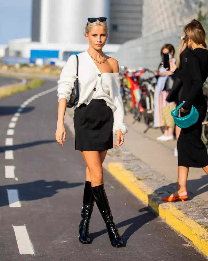 Девушка в черной мини юбке, белом кардигане и с мягкой мини сумочкой на плече