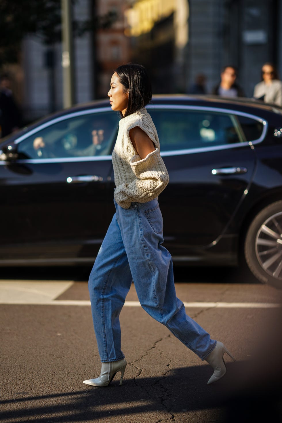 Девушка в мешковатых джинсах, свитере с вырезами на плечах и светлых ботильонах на шпильке