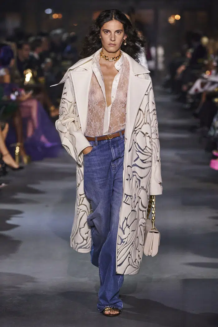 Модель в широких джинсах, блузке и белом пальто