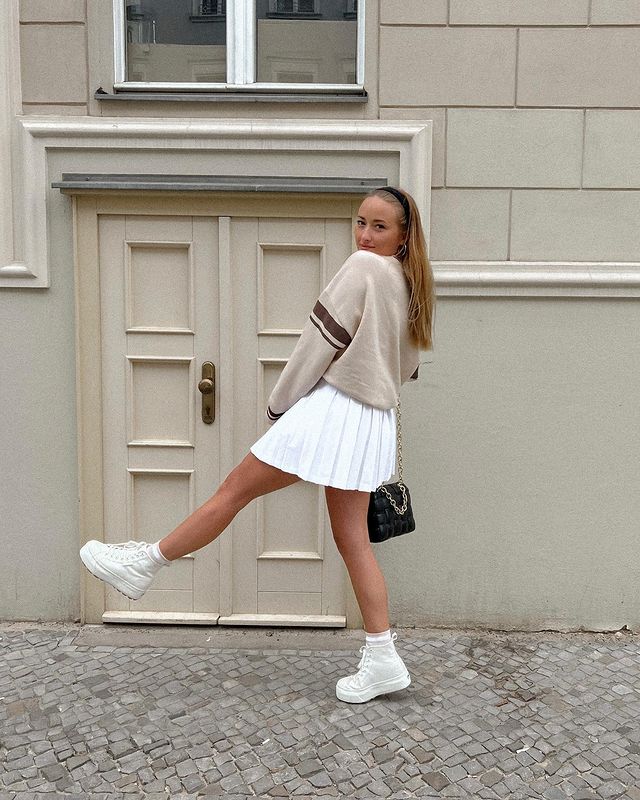 Девушка в белой мини юбке, свитшоте и белых высоких кроссовках