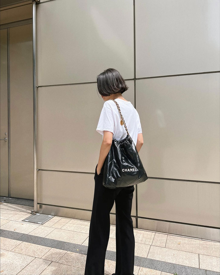 Девушка в белой футболке и черных брюках с большой мягкой сумкой от Chanel