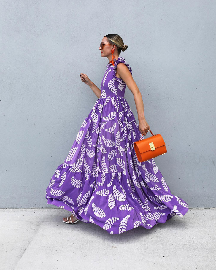 Девушка в просторном фиолетовом платье с белыми листьями и оранжевой сумочкой