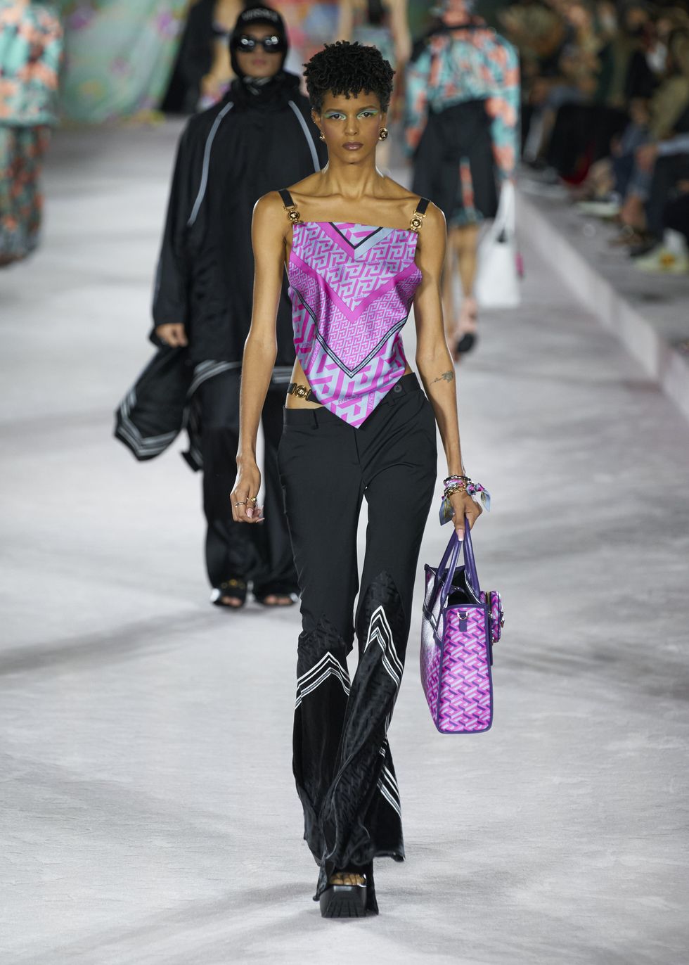 Модель в черных брюках клеш и розовом атласном топе от Versace