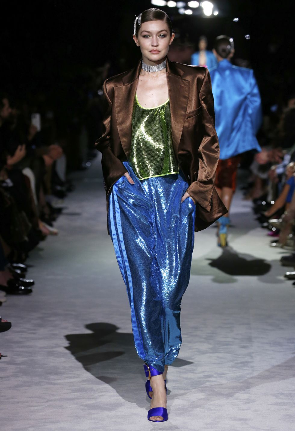 Модель в синих свободных штанах, блестящем зеленом топе и коричневом атласном блейзере от Tom Ford