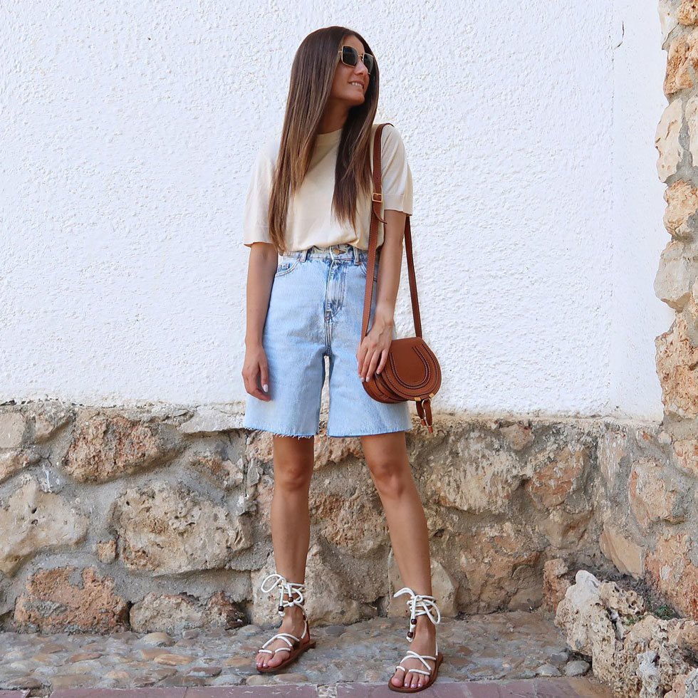Девушка в джинсовых бермудах, простой футболке и сандалиях на плоской подошве