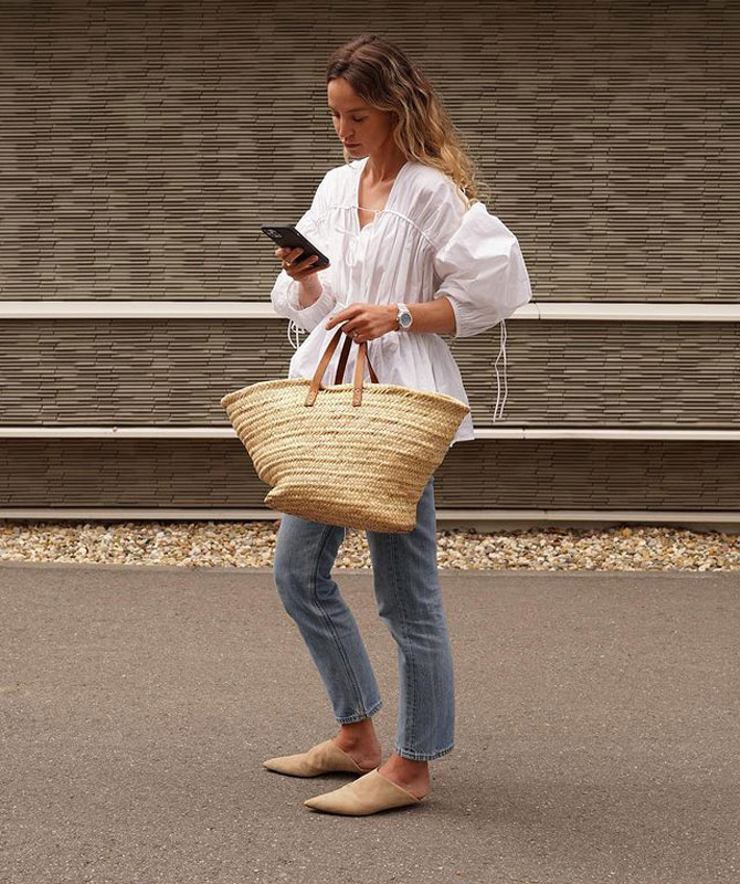 Девушка в укороченных джинсах, белой блузке и с соломенной сумкой