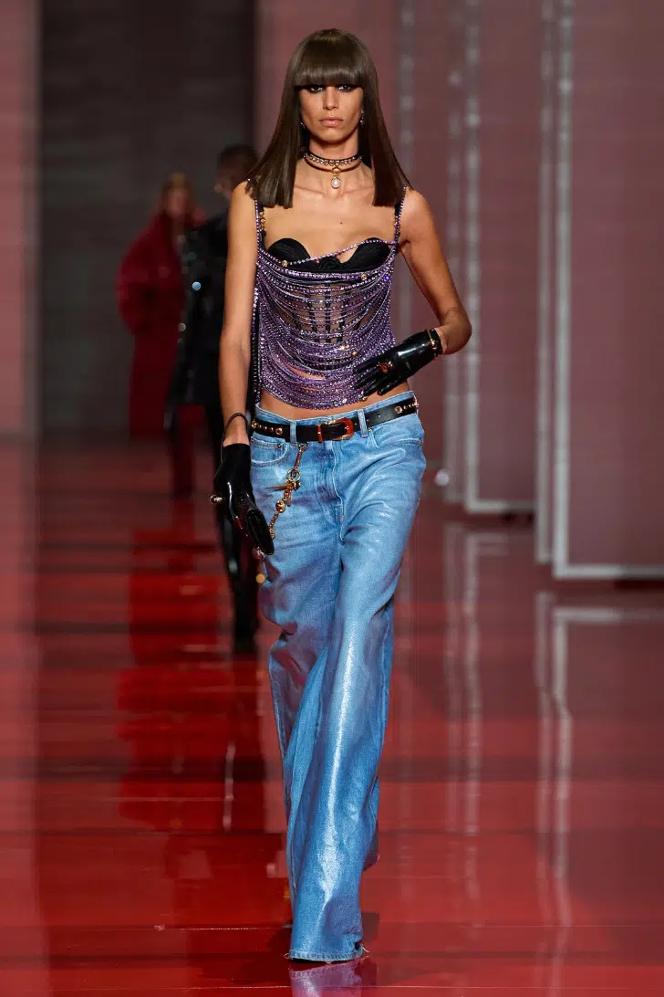 Модель в широких джинсах с низкой псадкой и блестящем топе от Versace