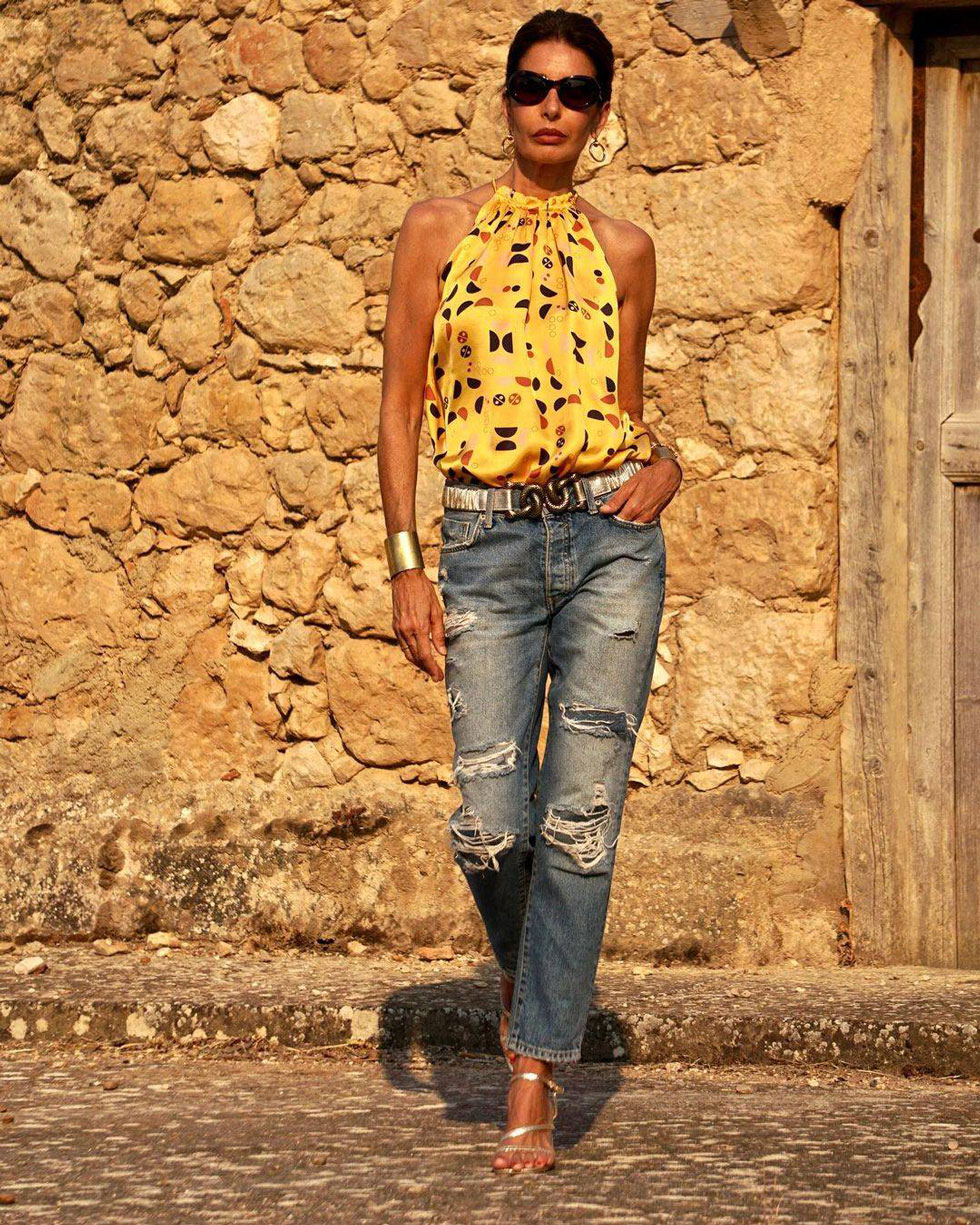 Женщина в рванных джинсах, желтом топе с принтом и серебристых босоножках на каблуке