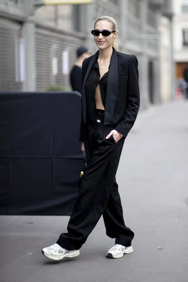 Девушка в черном костюме со свободными брюками и белых кроссовках