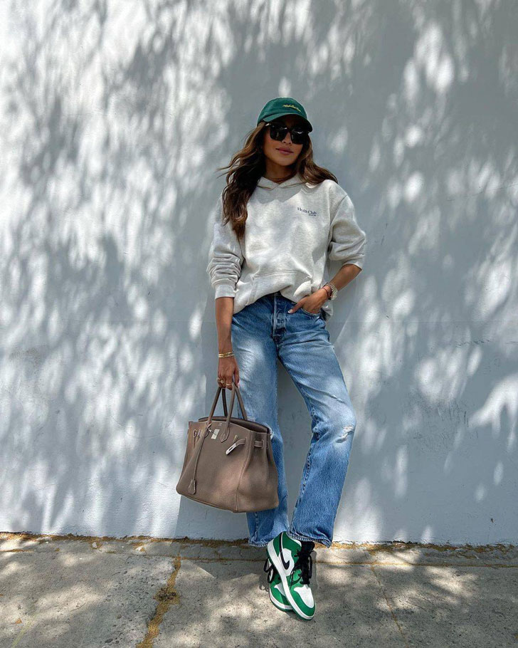 Девушка в простых джинсах, серой толстовке и бело зеленых кроссовках