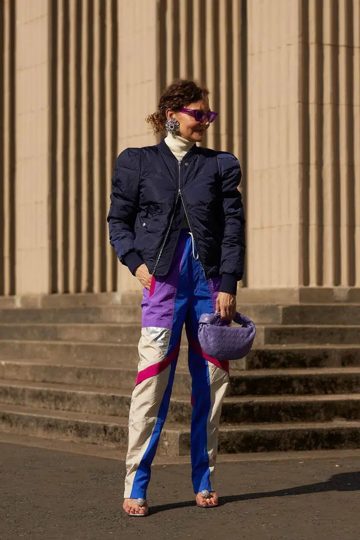 Женщина в ярких разноцветных брюках карго, синем бомбере и босоножках на каблуке