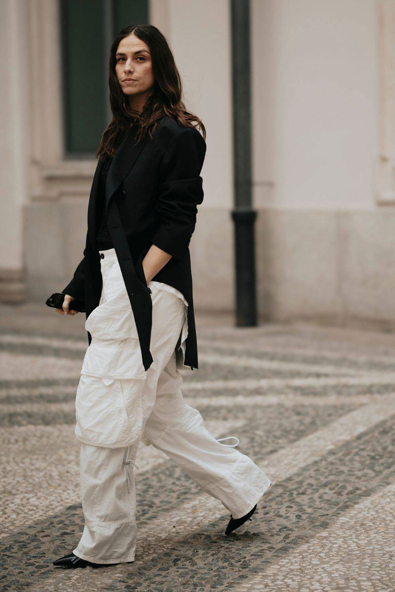 Женщина в белых брюках карго, черном блейзере и лакированных туфлях