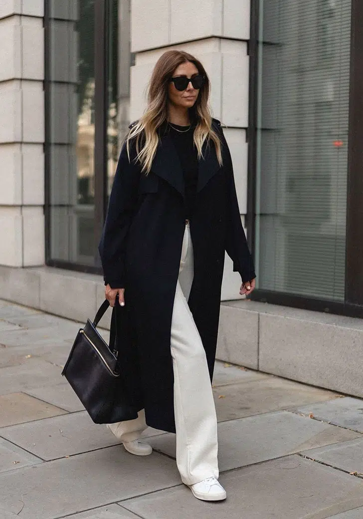 Девушка в белых свободных брюках, черном длинном пальто и кедах